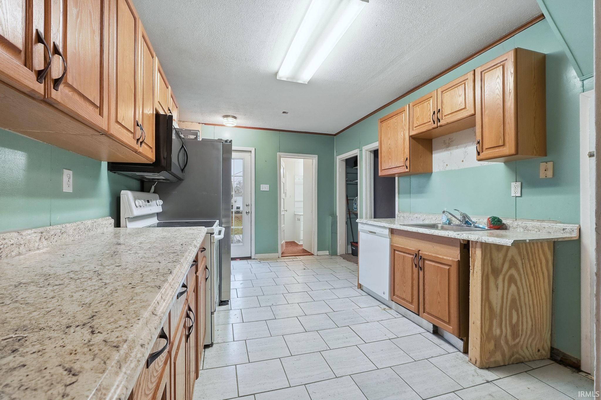 Kitchen featuring white appliances, ornamental molding, a textured ceiling, and light stone countertops