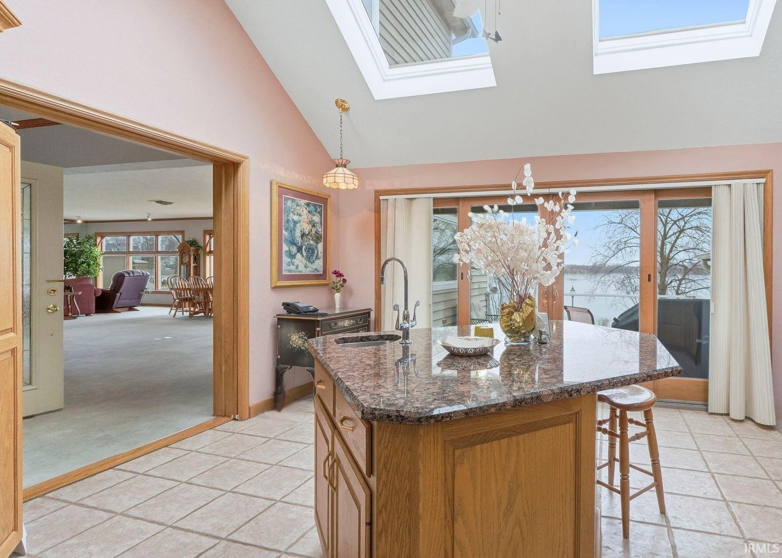 Kitchen featuring dark stone countertops, lofted ceiling, brown cabinetry, pendant lighting, and a skylight