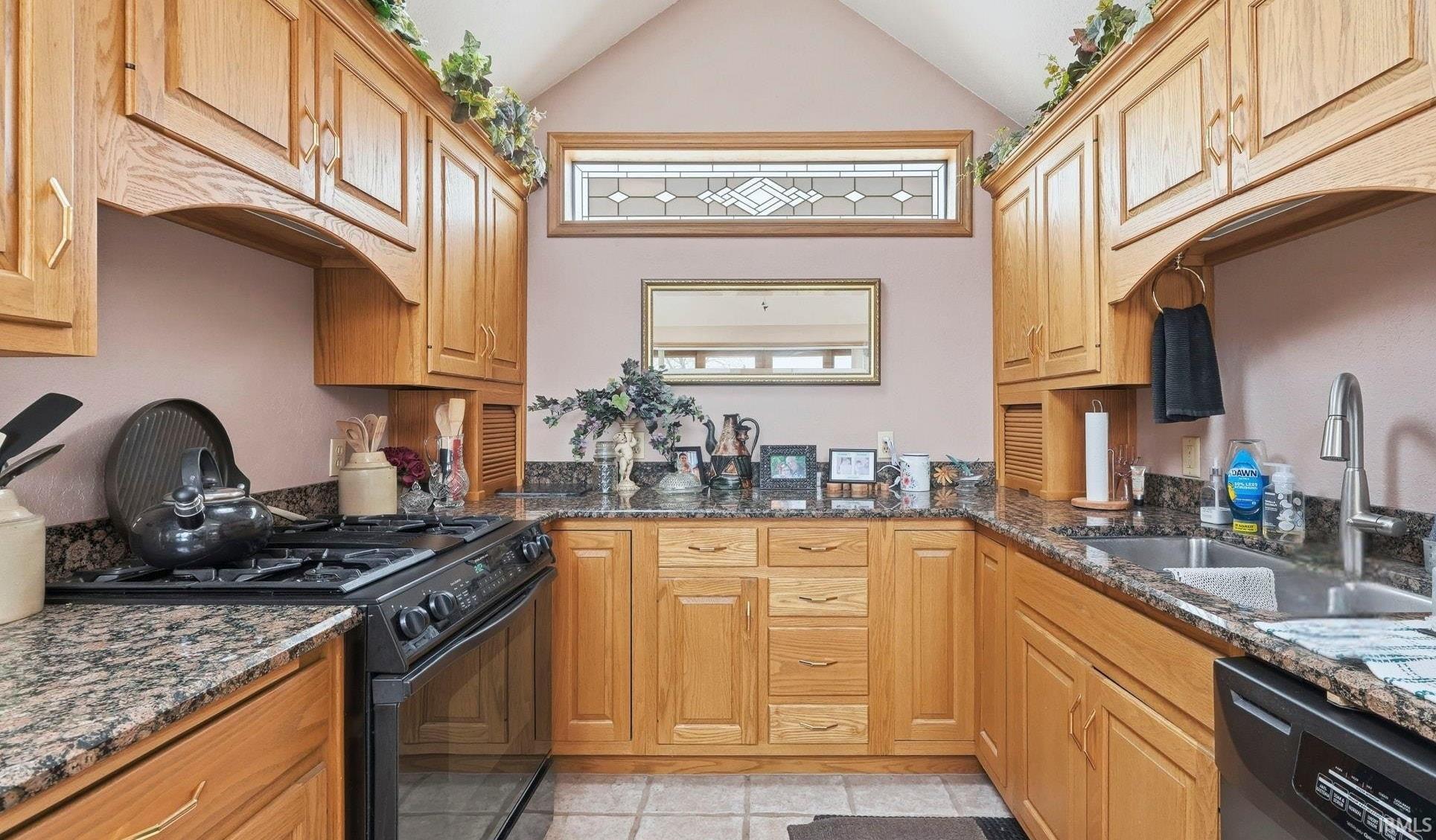 Kitchen with black appliances, dark stone countertops, under cabinet range hood, lofted ceiling, and light tile patterned floors