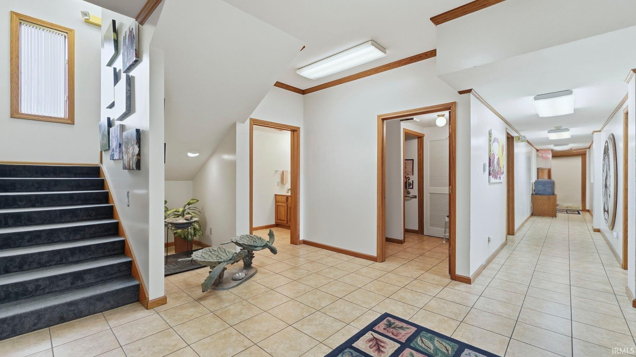 Hall with light tile patterned flooring, ornamental molding, and stairway