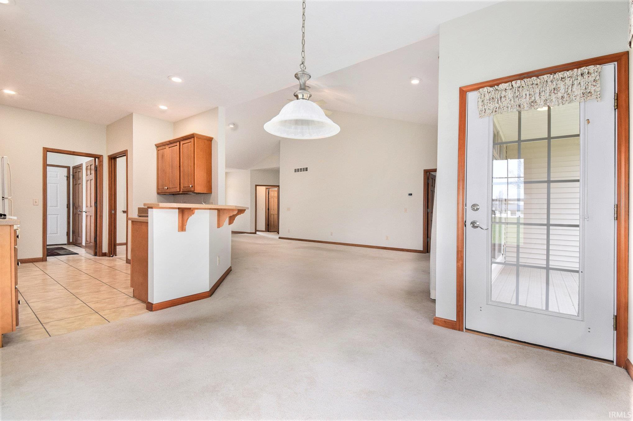 Kitchen featuring light carpet, a breakfast bar, brown cabinets, lofted ceiling, and hanging light fixtures