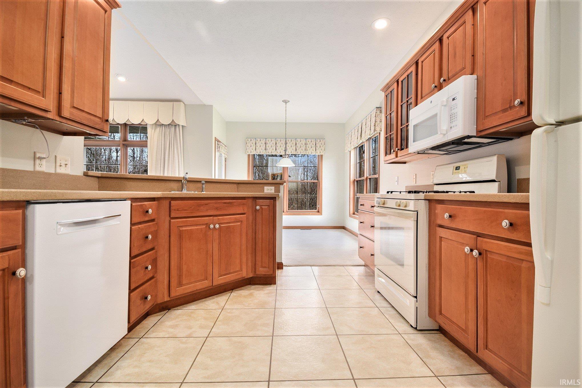 Kitchen featuring brown cabinets, white appliances, a peninsula, decorative light fixtures, and recessed lighting