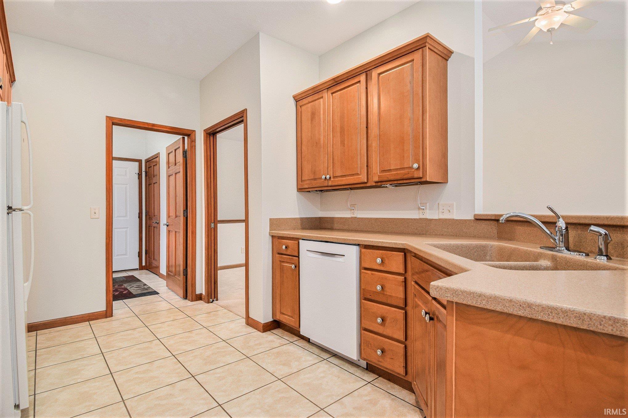 Kitchen with white appliances, light tile patterned floors, brown cabinetry, and light stone countertops