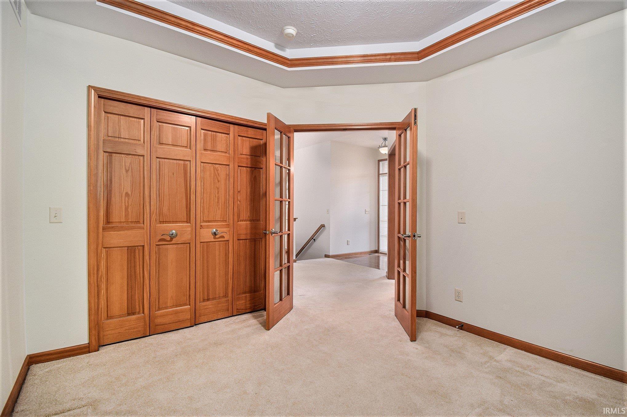Unfurnished bedroom with light carpet, french doors, a closet, and a textured ceiling