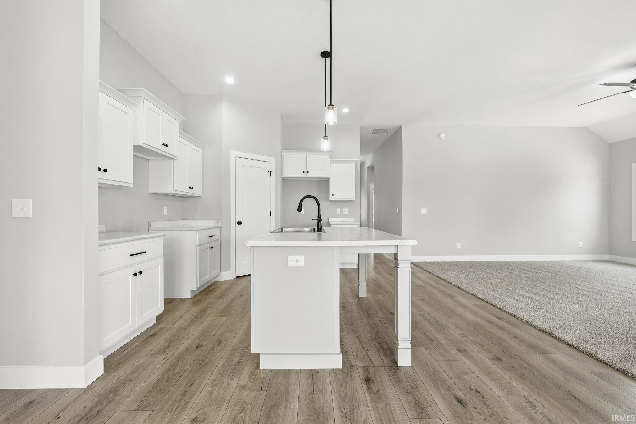 Kitchen featuring a breakfast bar, white cabinetry, pendant lighting, an island with sink, and light wood-style flooring