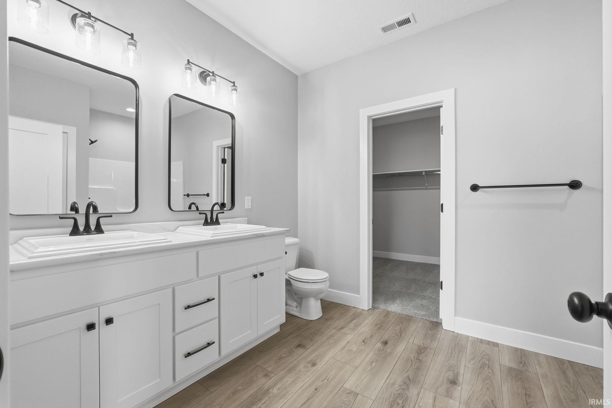 Bathroom with double vanity, light wood-style floors, and a walk in closet