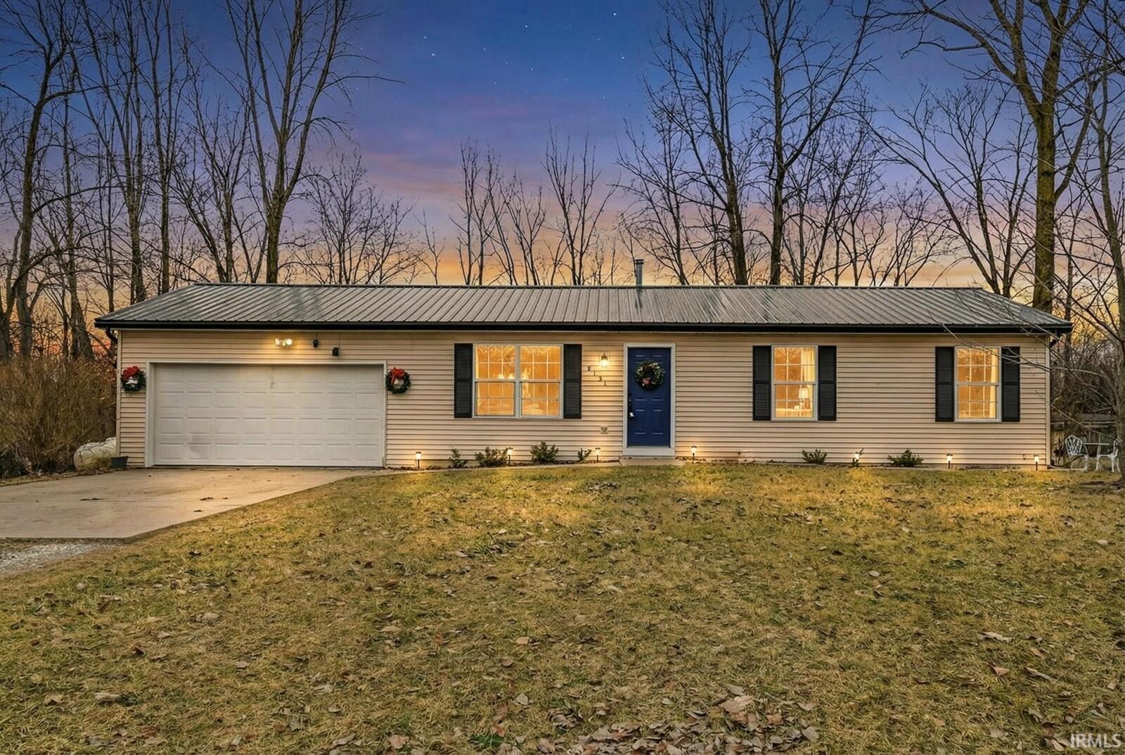 Ranch-style home featuring concrete driveway, a garage, a metal roof, and a front yard