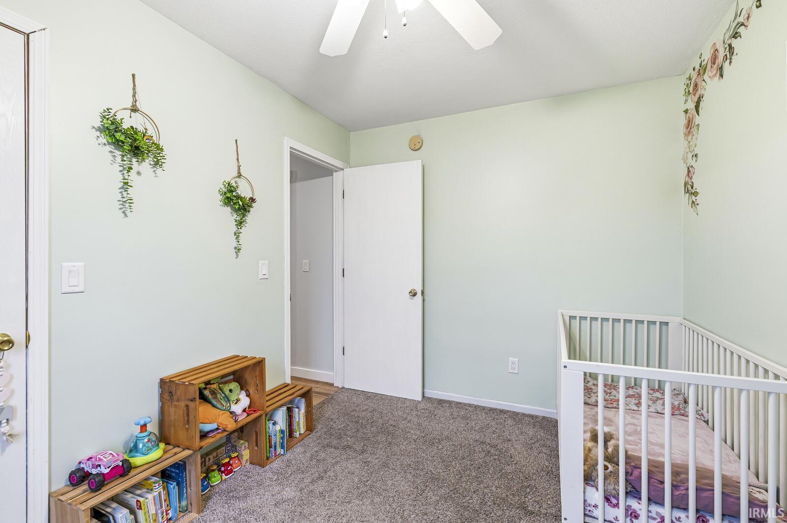 Carpeted bedroom with a crib and a ceiling fan
