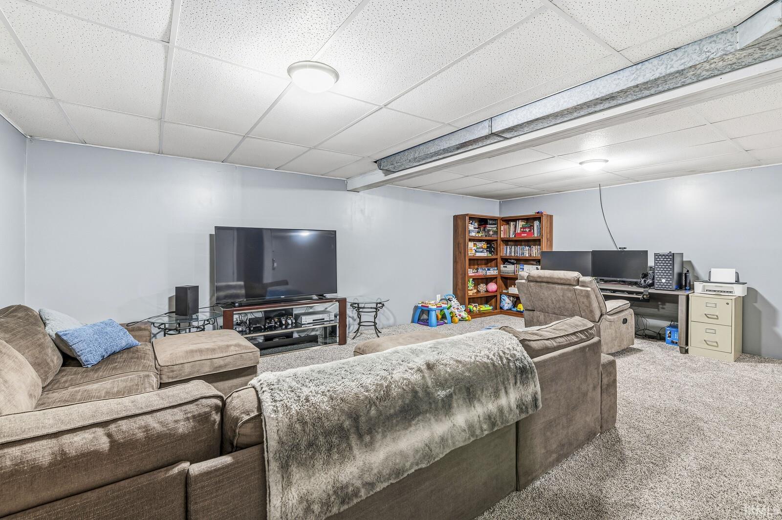 Living area with carpet, a paneled ceiling, and a desk