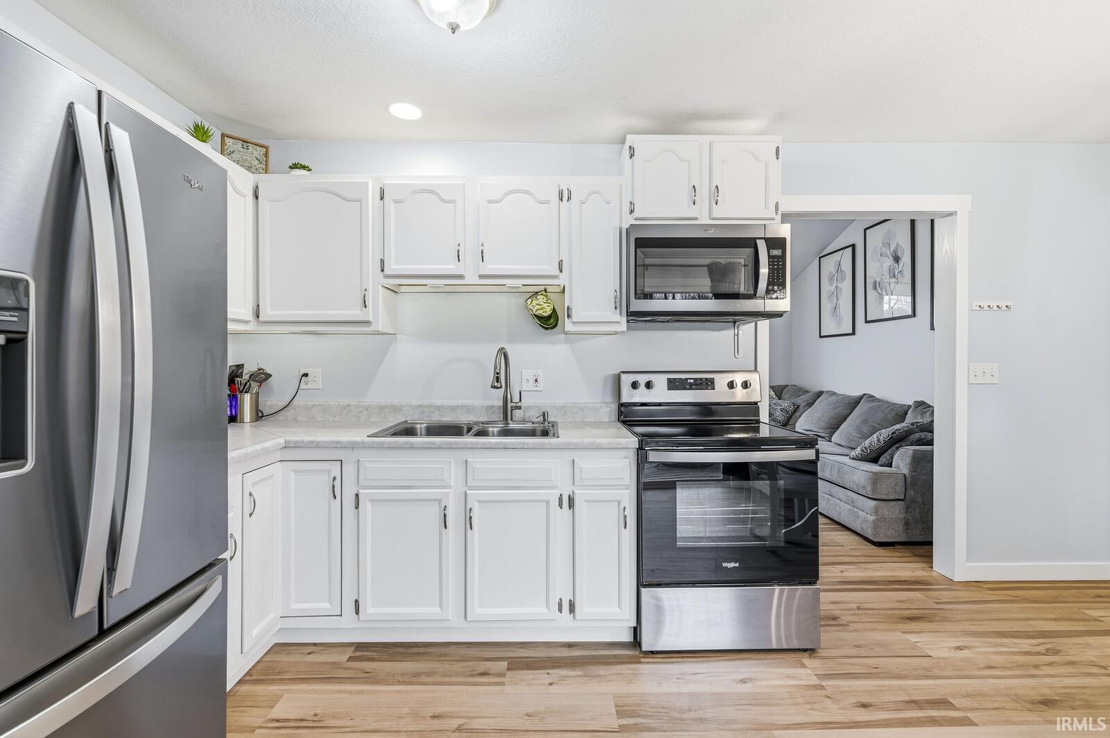 Kitchen featuring appliances with stainless steel finishes, white cabinets, light countertops, light wood-style floors, and recessed lighting