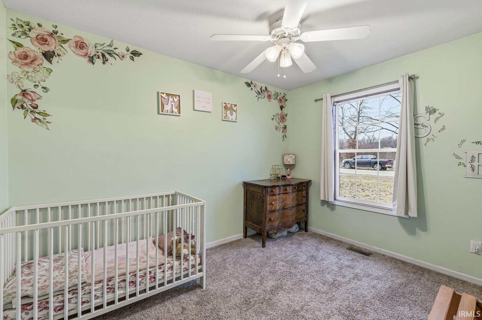 Carpeted bedroom with a crib and ceiling fan