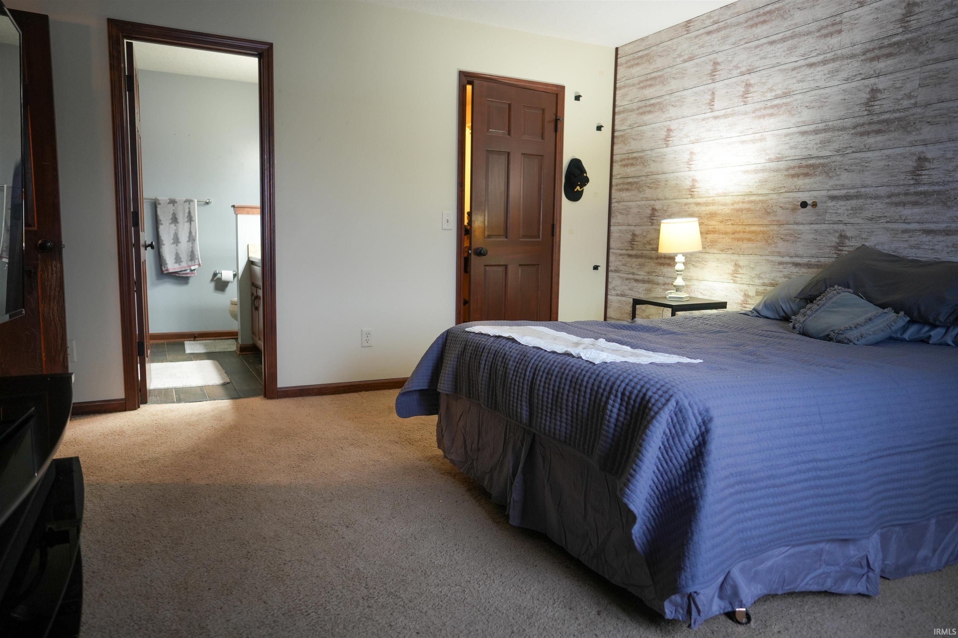 Carpeted bedroom featuring wood walls, an accent wall, and ensuite bathroom