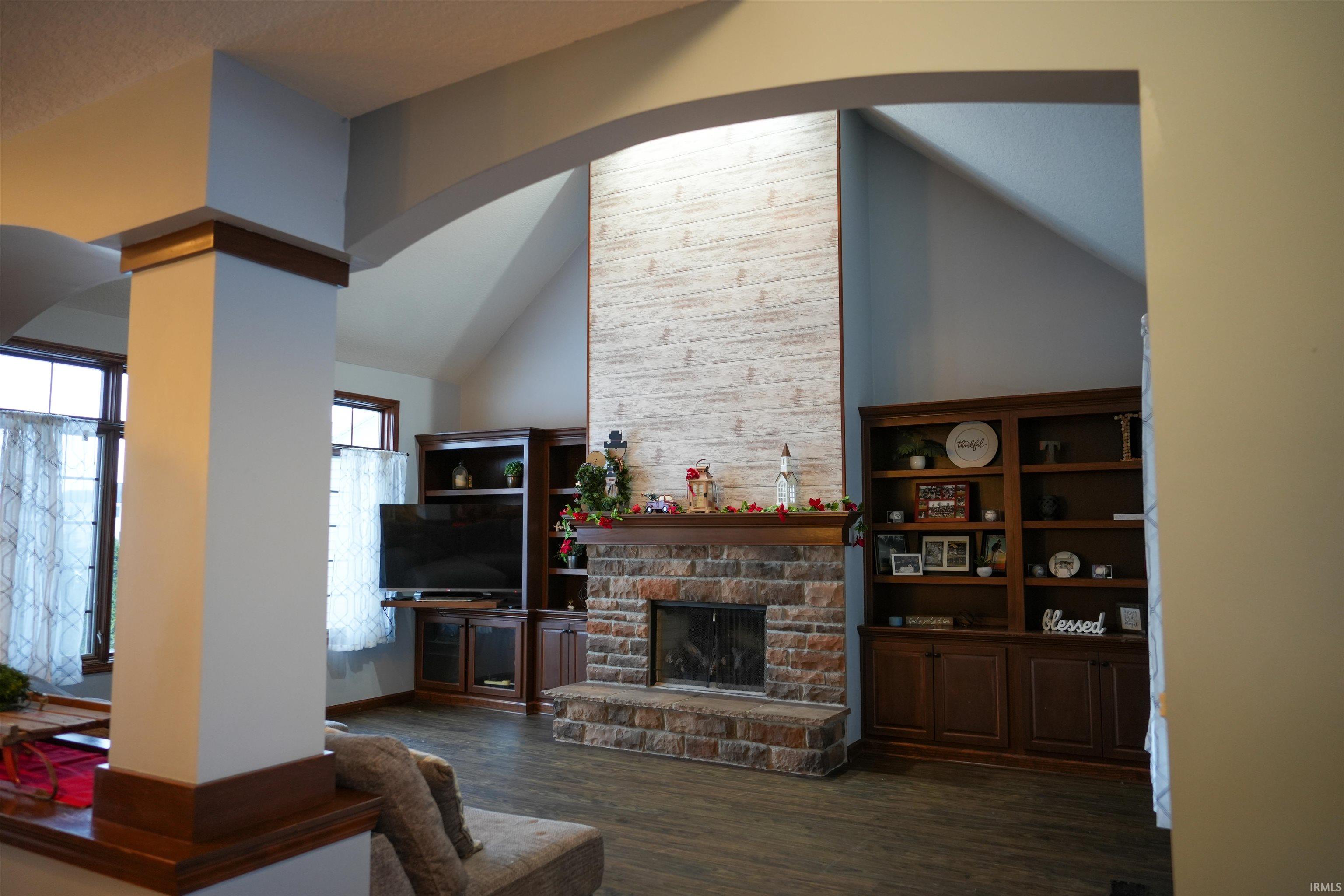 Living room with dark wood-style floors, arched walkways, a stone fireplace, and high vaulted ceiling