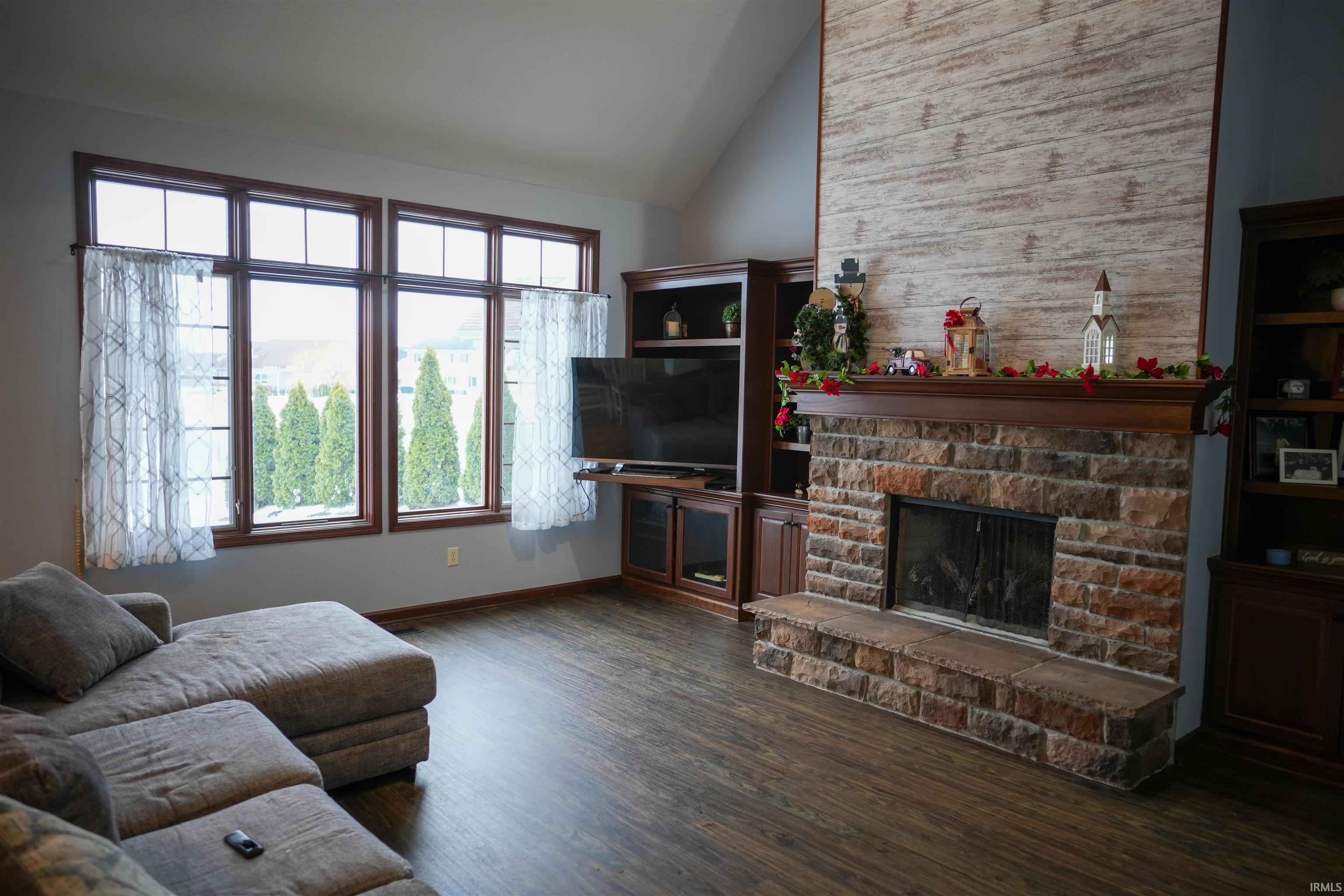 Living room with dark wood-type flooring, lofted ceiling, and a stone fireplace
