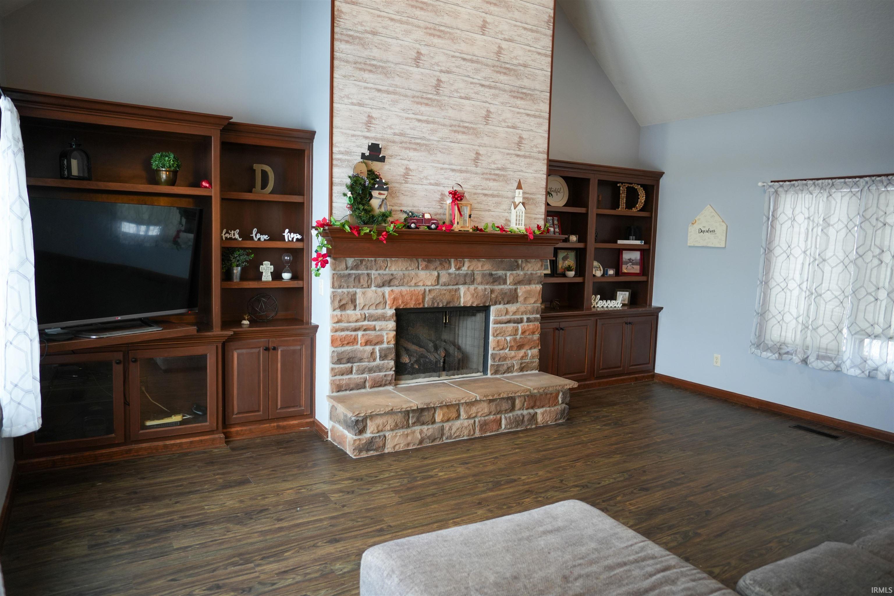 Living area with dark wood finished floors, a stone fireplace, and high vaulted ceiling