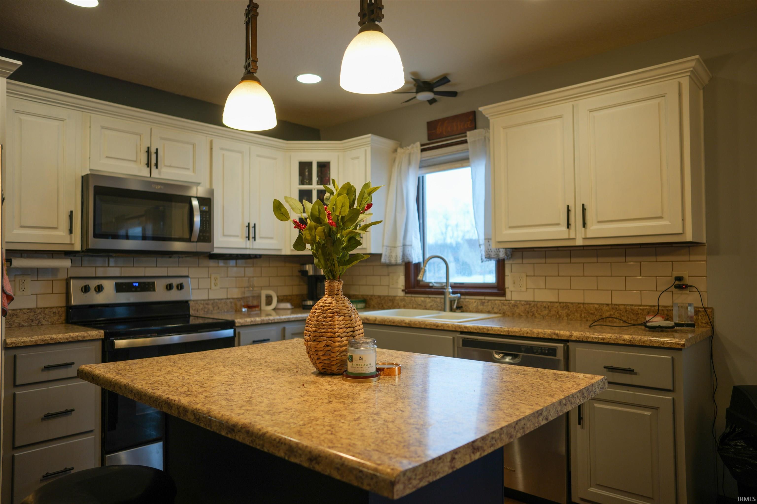 Kitchen with a center island, stainless steel appliances, pendant lighting, light countertops, and glass insert cabinets