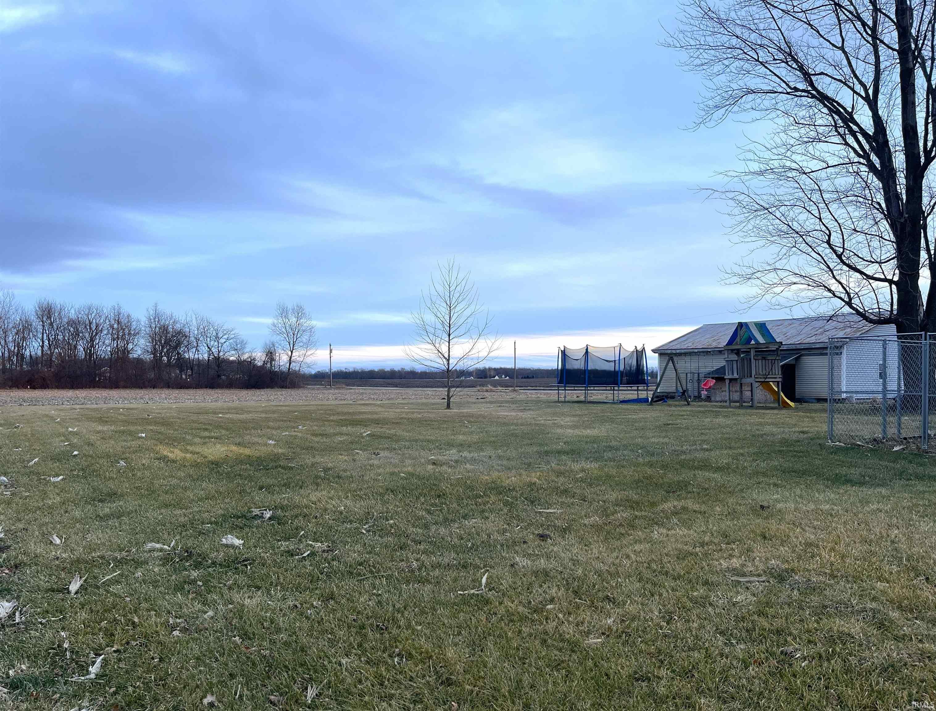 View of green lawn with a trampoline, a view of rural / pastoral area, and a playground