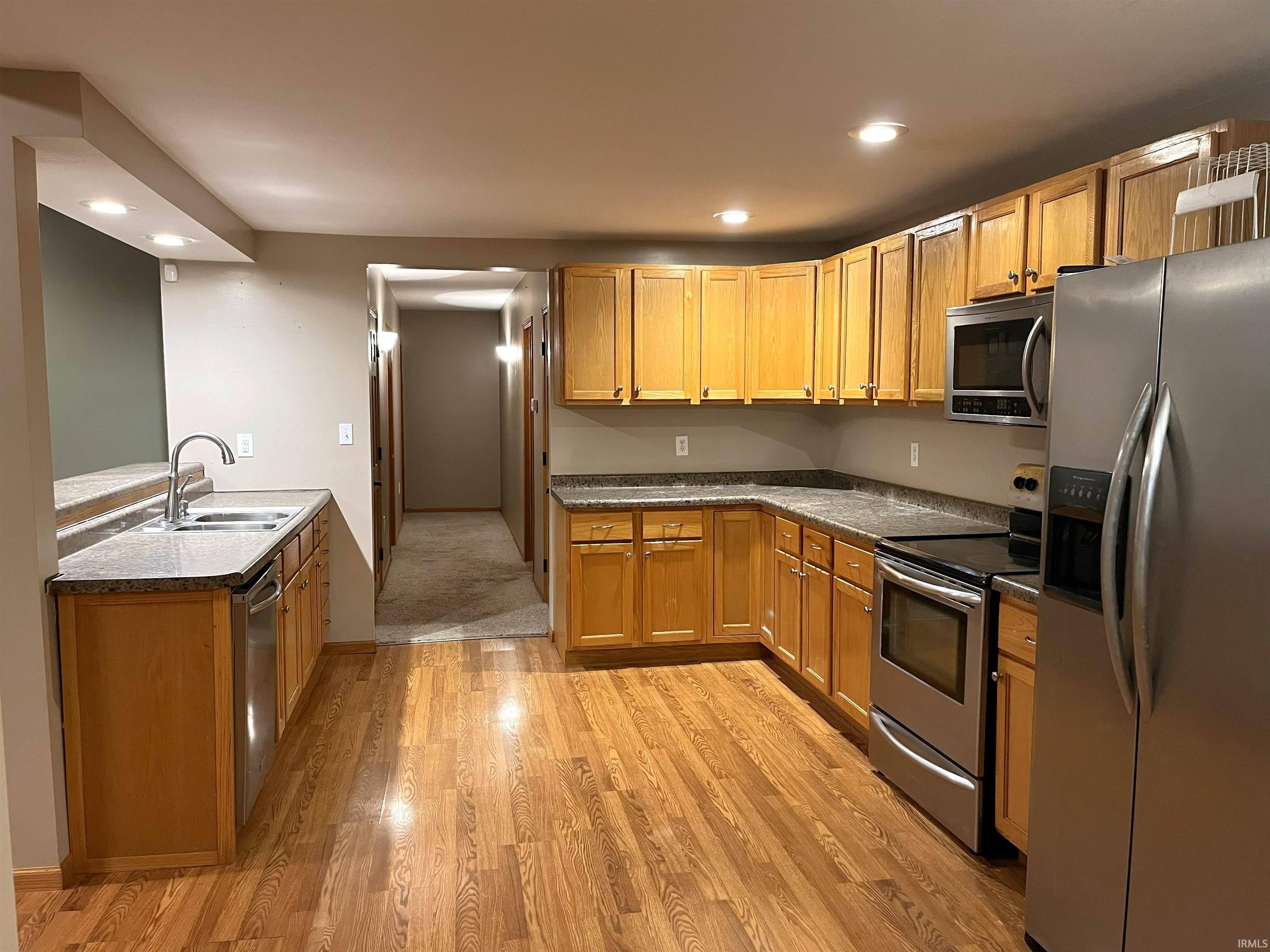 Kitchen with appliances with stainless steel finishes, recessed lighting, light wood finished floors, brown cabinets, and a peninsula