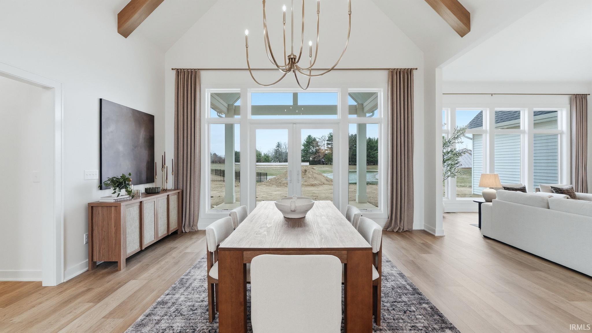 Dining space with hanging lights, lofted ceiling, light wood-style floors, and french doors