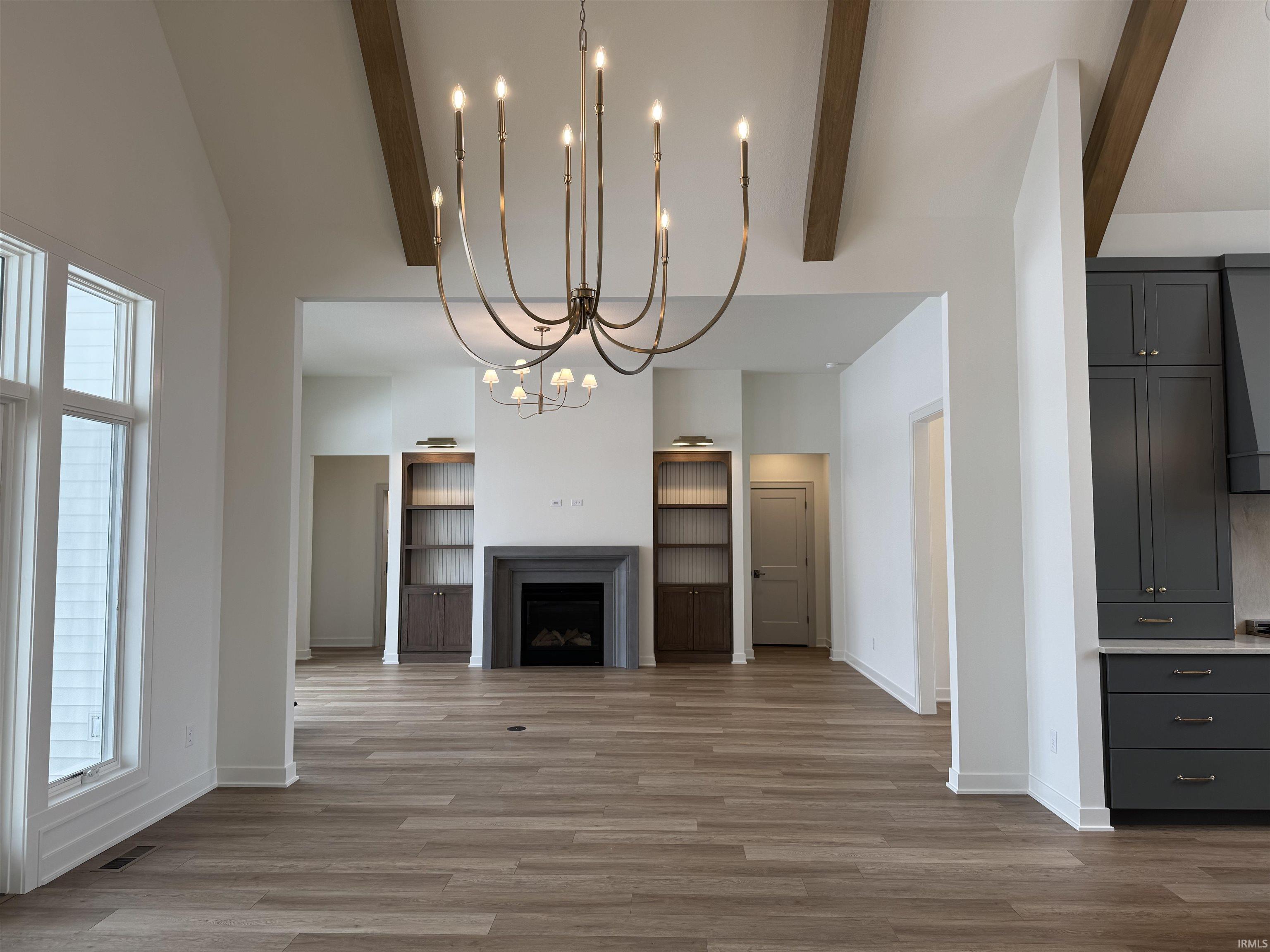 Unfurnished living room featuring suspended lighting, vaulted ceiling, a fireplace, light wood finished floors, and built in shelves
