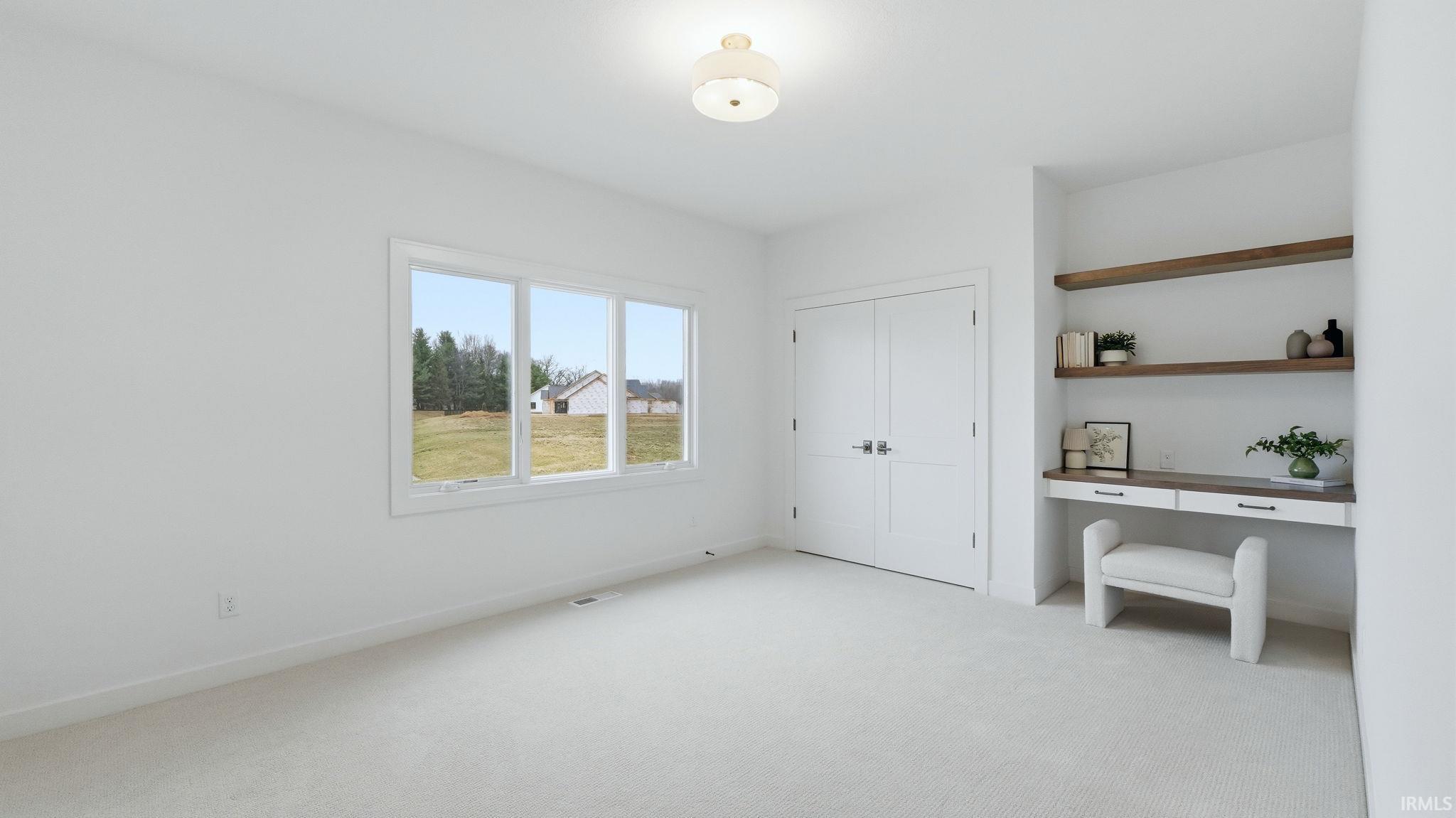 Unfurnished bedroom featuring built in desk, light colored carpet, and a closet