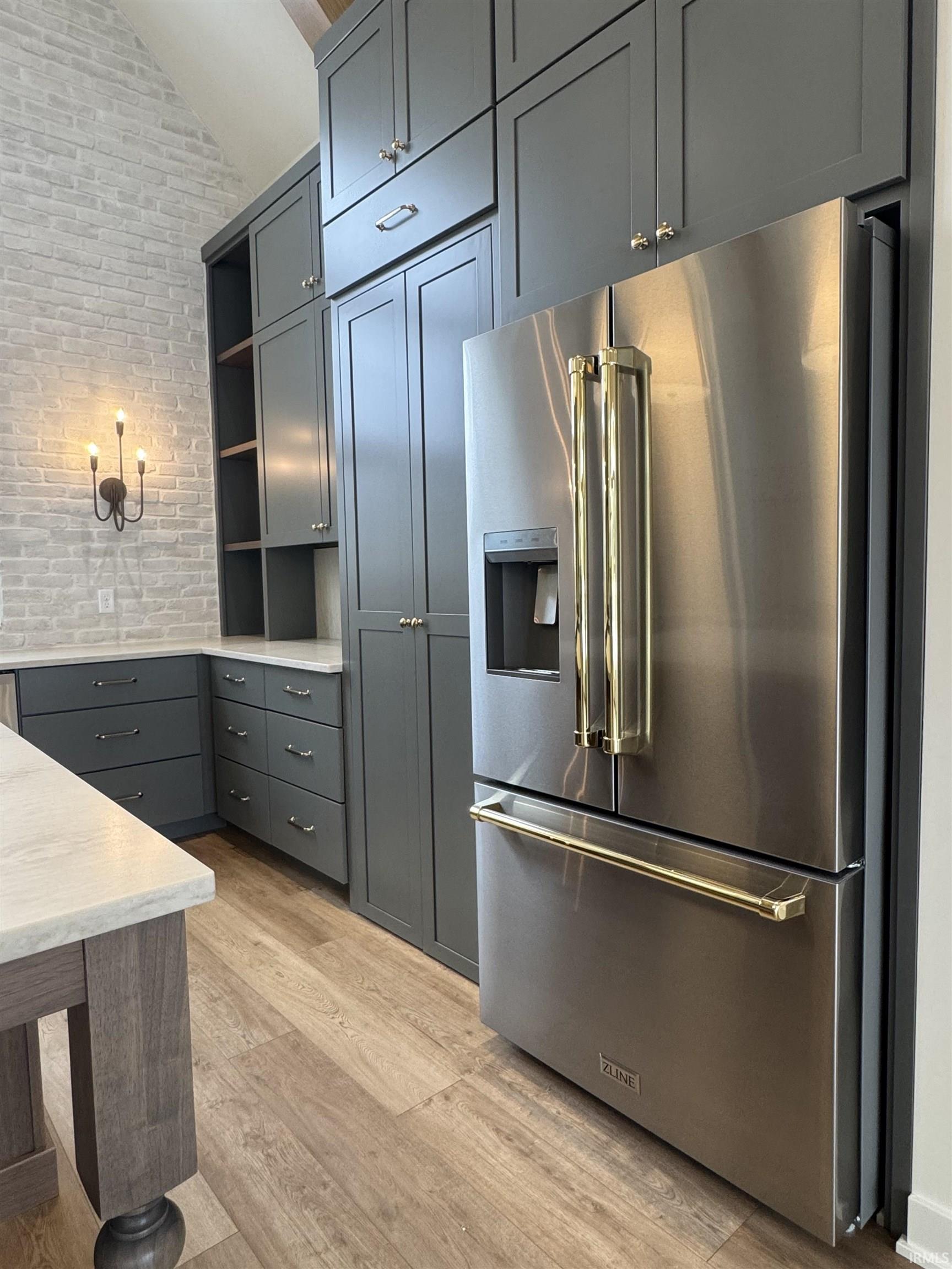 Kitchen with high end refrigerator, brick wall, gray cabinetry, light wood-style flooring, and lofted ceiling