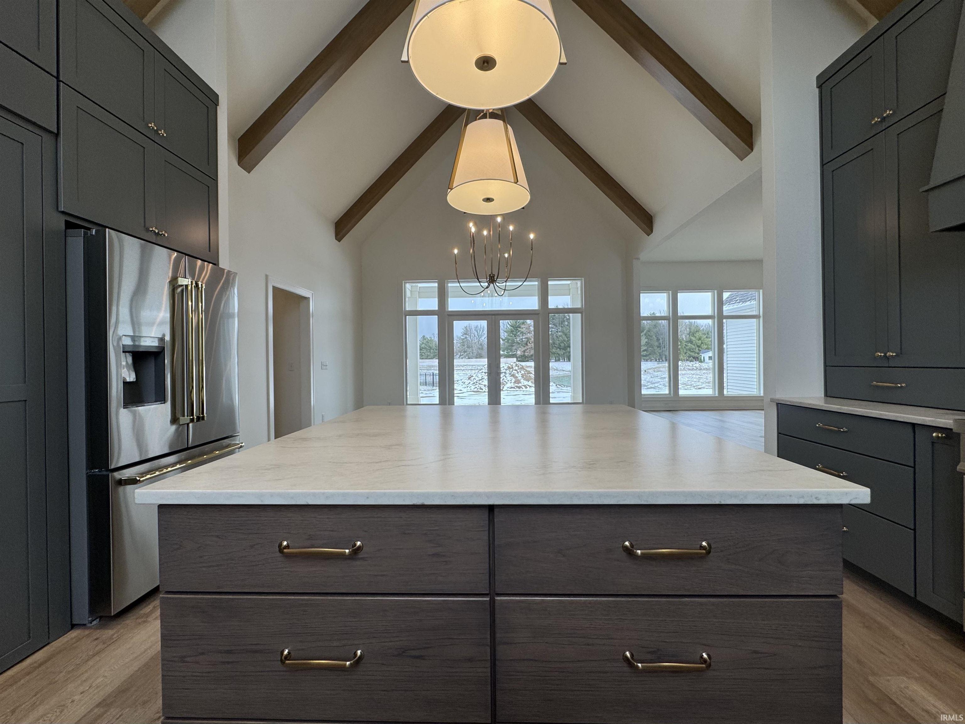 Kitchen with a large island, high end refrigerator, dark wood finish cabinetry, lofted ceiling, and light wood-style flooring