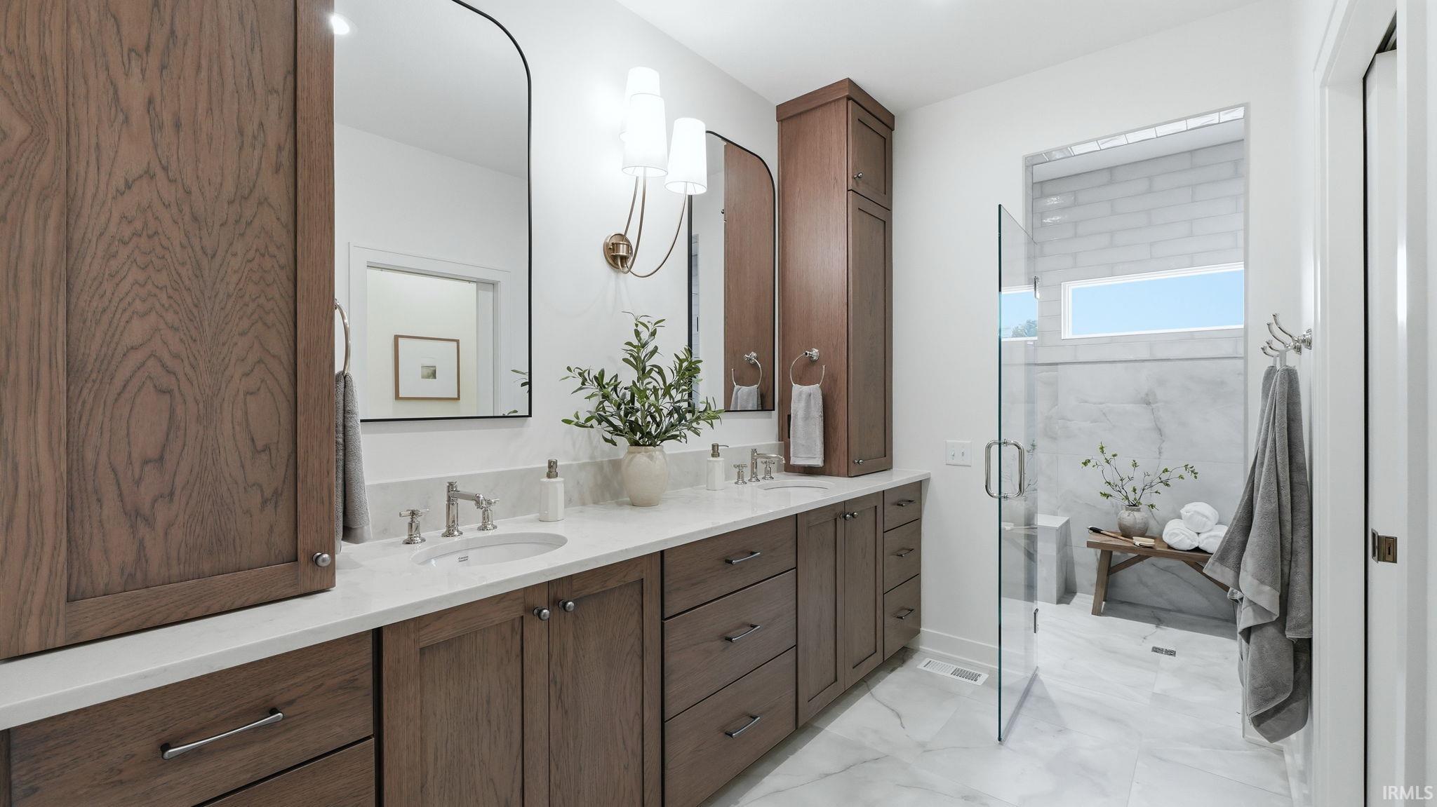 Full bath with double vanity, a marble finish shower, and light marble finish floors