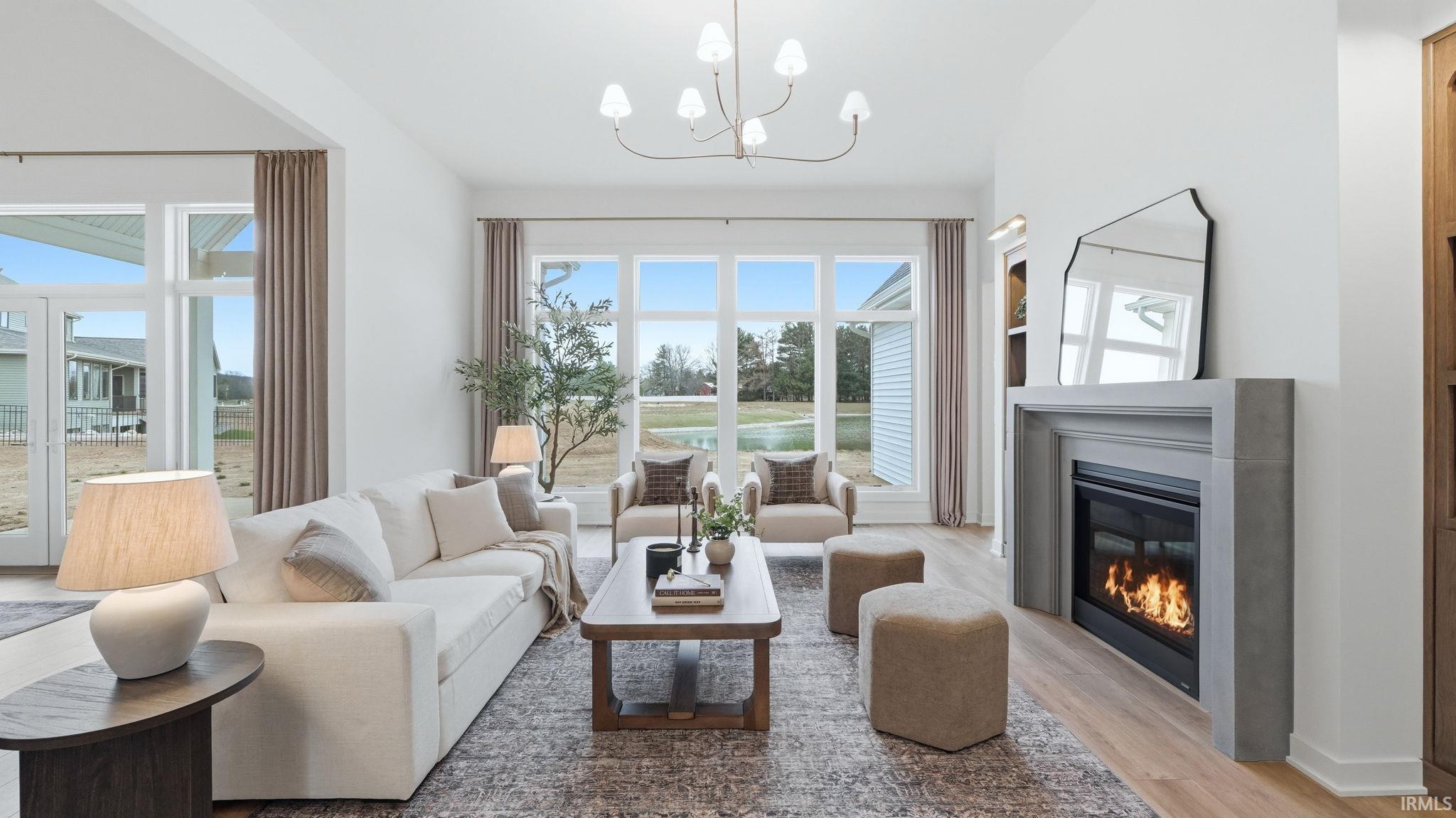 Living room featuring light wood-style floors, a glass covered fireplace, a chandelier, and vaulted ceiling