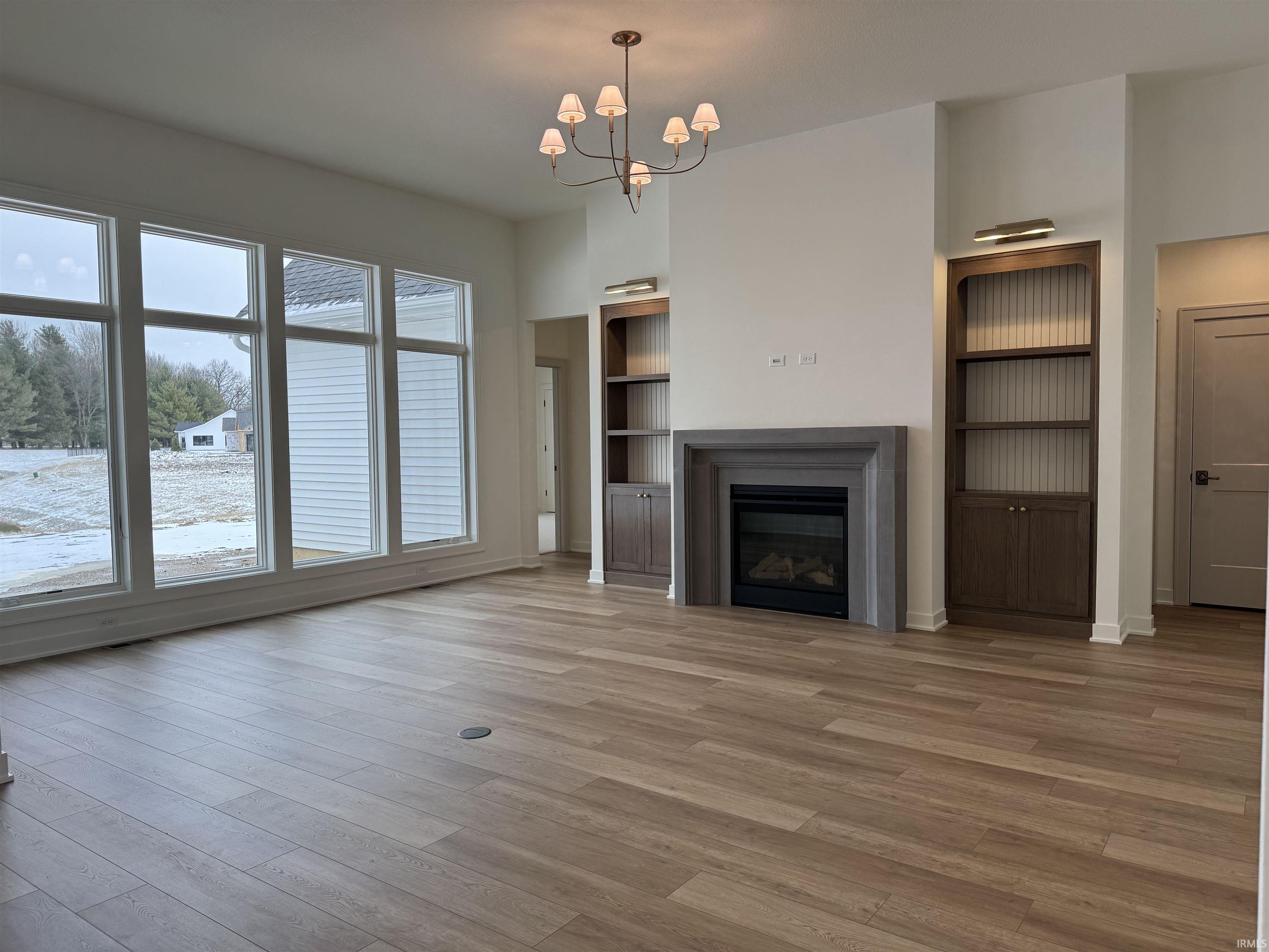 Unfurnished living room with hanging lights, built in features, light wood-type flooring, and a glass covered fireplace