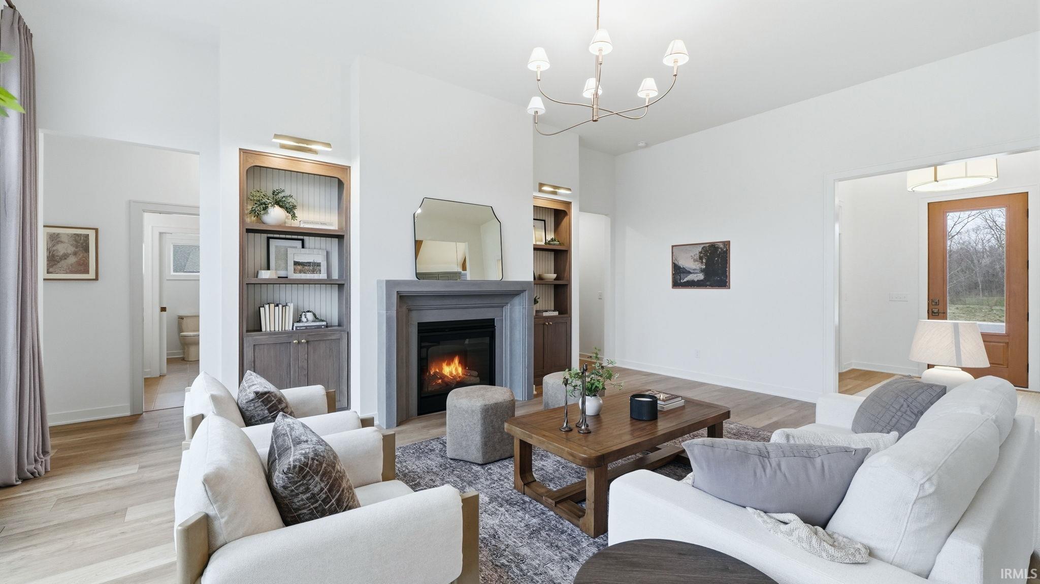 Living area featuring built in shelves, light wood finished floors, a chandelier, and a glass covered fireplace