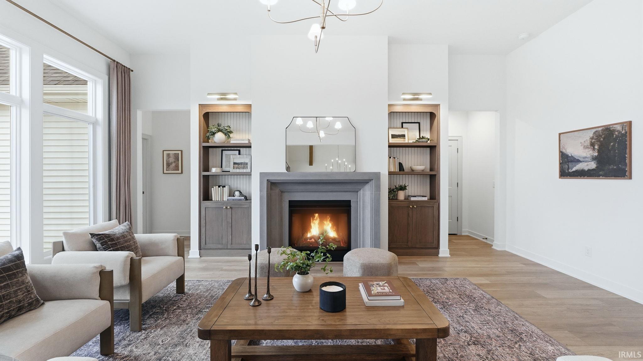 Living room featuring light wood-style floors, a chandelier, a lit fireplace, and built in shelves