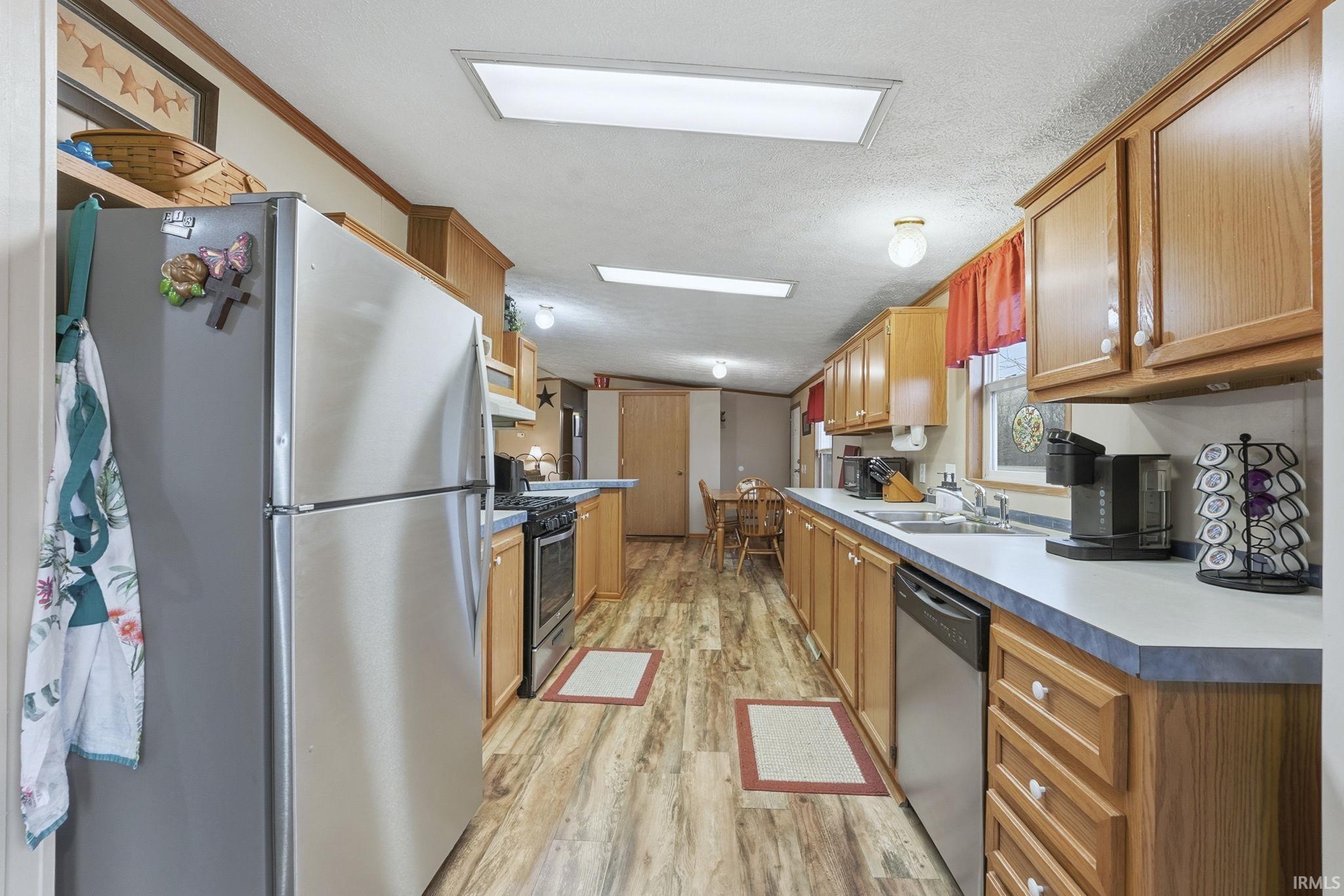 Kitchen featuring appliances with stainless steel finishes, light wood-style floors, brown cabinets, vaulted ceiling, and light countertops