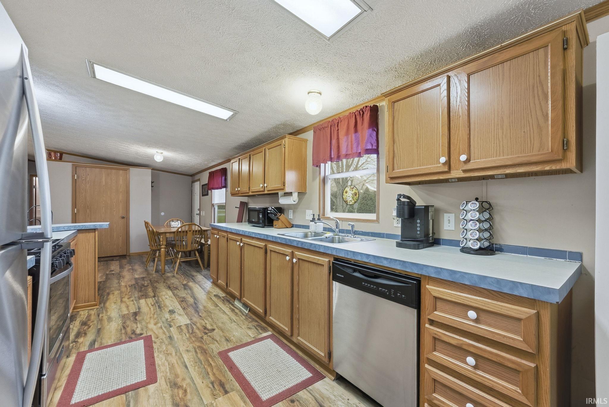 Kitchen featuring vaulted ceiling, appliances with stainless steel finishes, light wood-type flooring, light countertops, and a textured ceiling