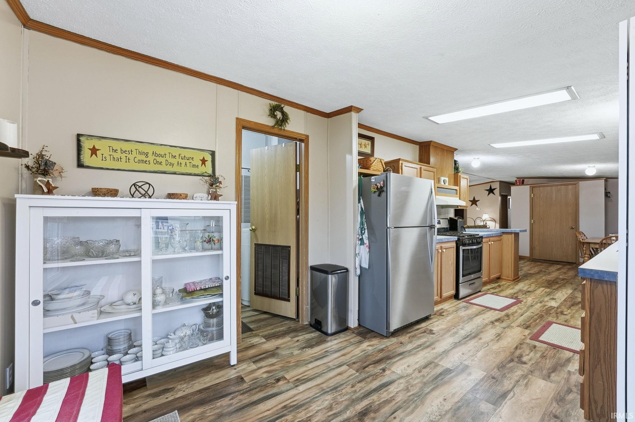 Kitchen with stainless steel appliances, crown molding, light wood-style floors, a textured ceiling, and under cabinet range hood