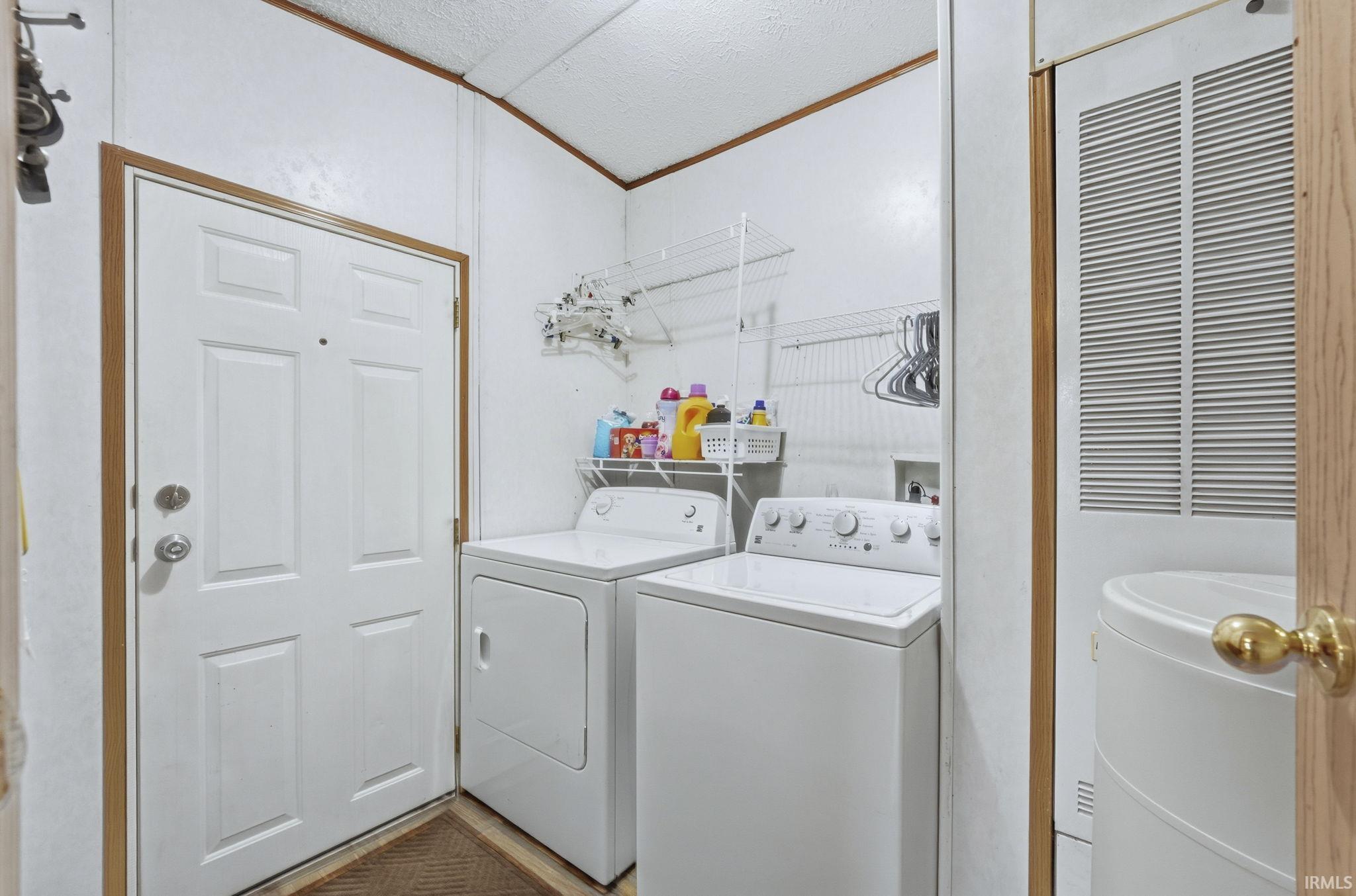 Laundry room with a heating unit, washer and dryer, ornamental molding, vaulted ceiling, and a textured ceiling