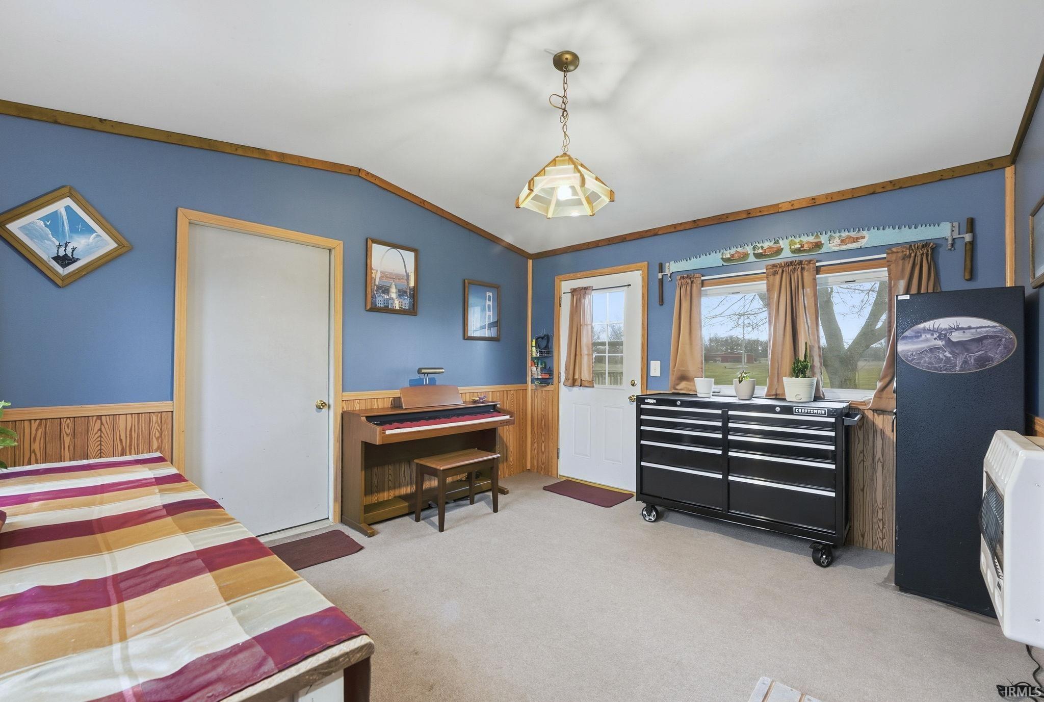 Bedroom featuring light carpet, vaulted ceiling, wood walls, wainscoting, and heating unit