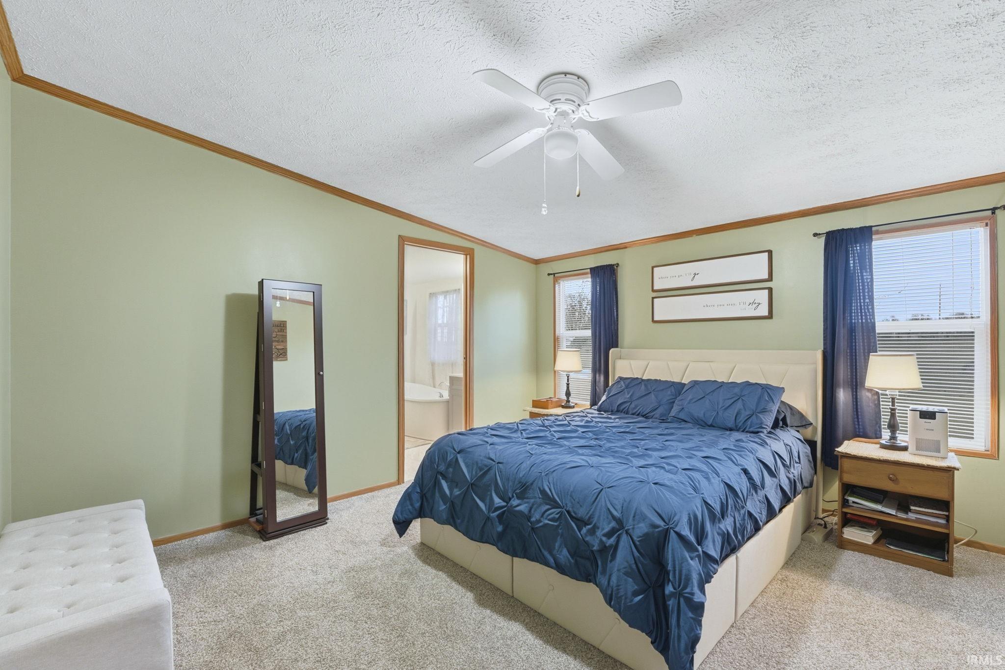 Carpeted bedroom with crown molding, a textured ceiling, ensuite bathroom, and ceiling fan