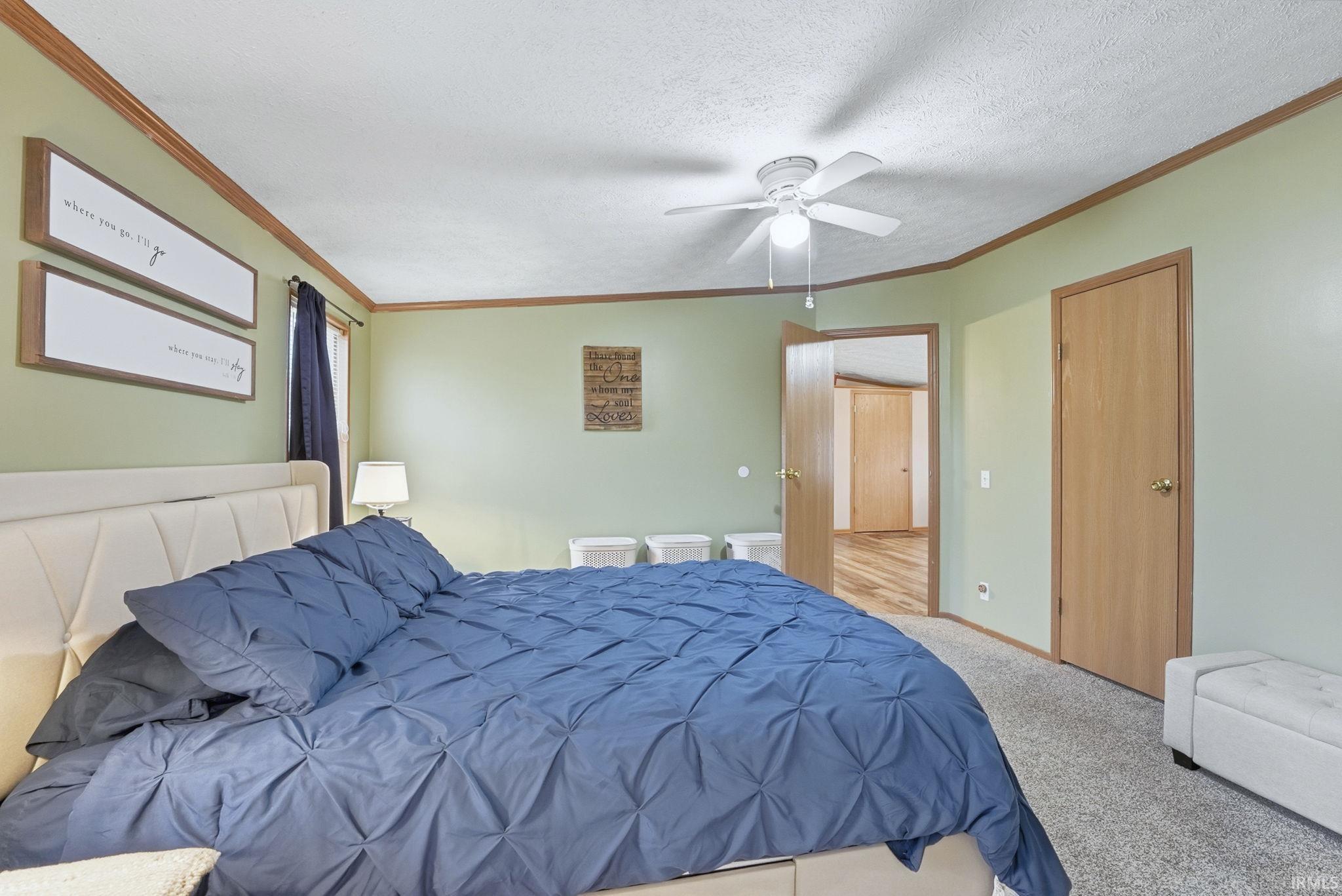 Bedroom with ornamental molding, carpet, a ceiling fan, and a textured ceiling