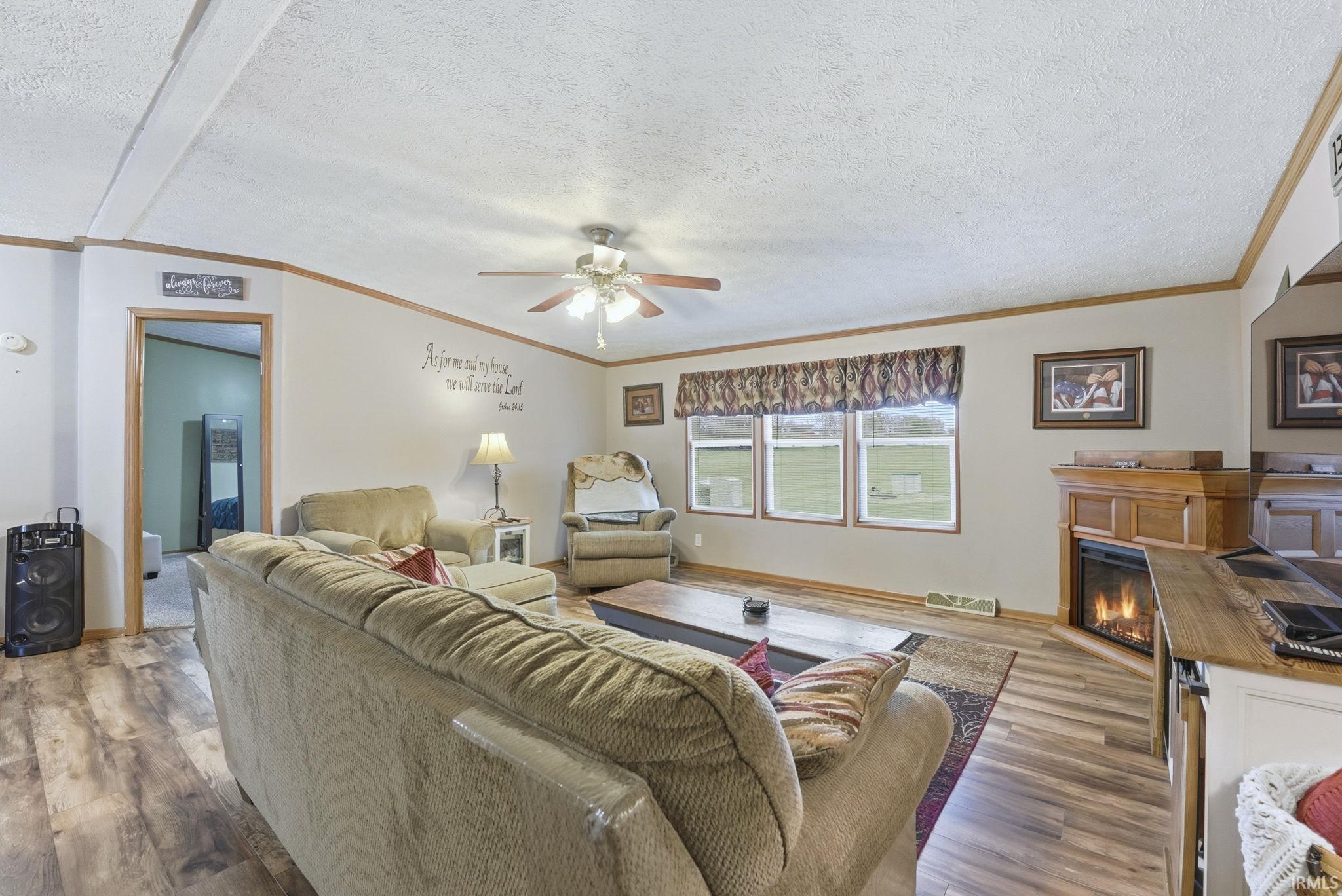 Living room with a glass covered fireplace, ornamental molding, wood finished floors, a textured ceiling, and ceiling fan