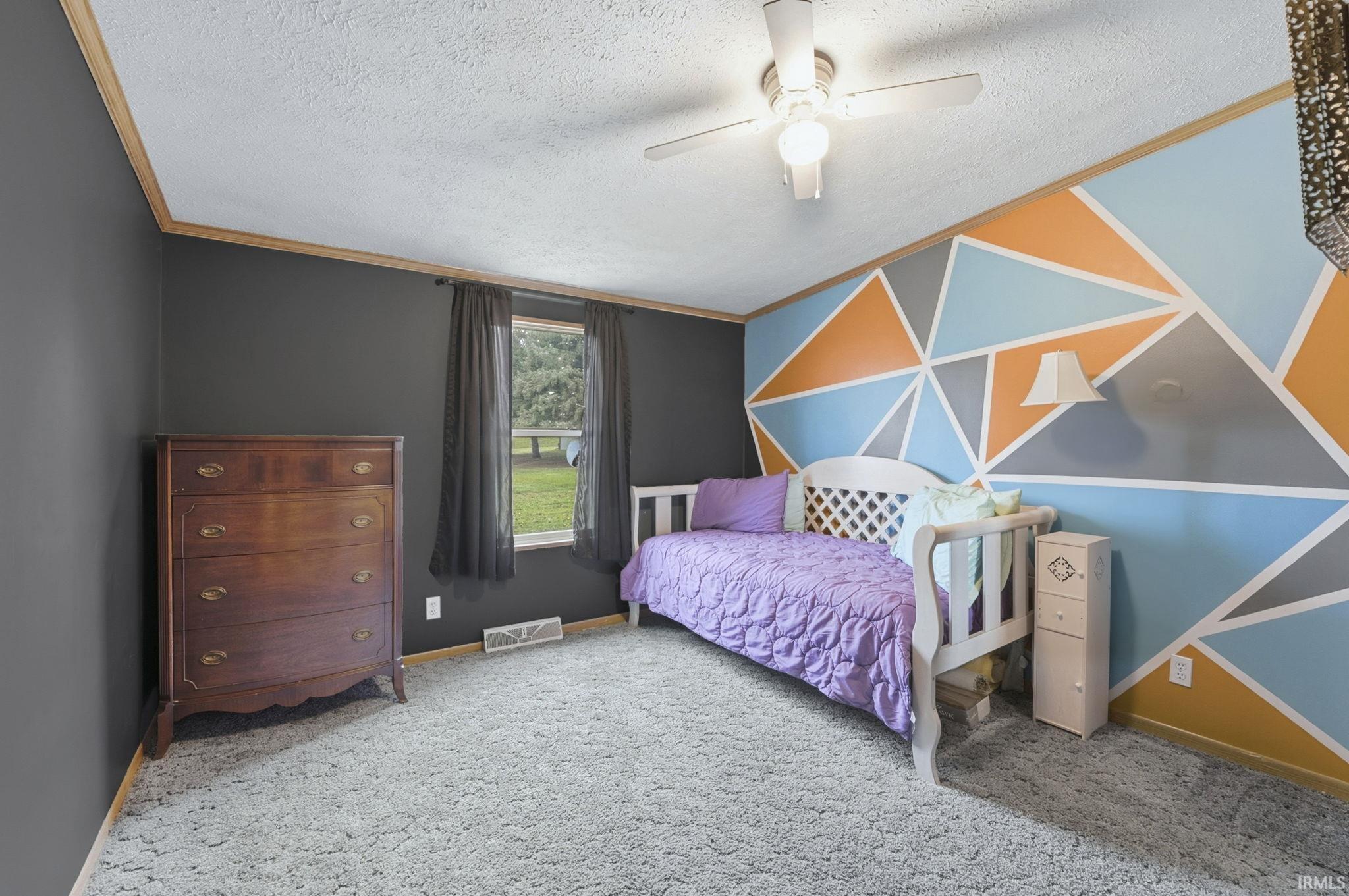 Carpeted bedroom with a ceiling fan, a textured ceiling, crown molding, and an accent wall