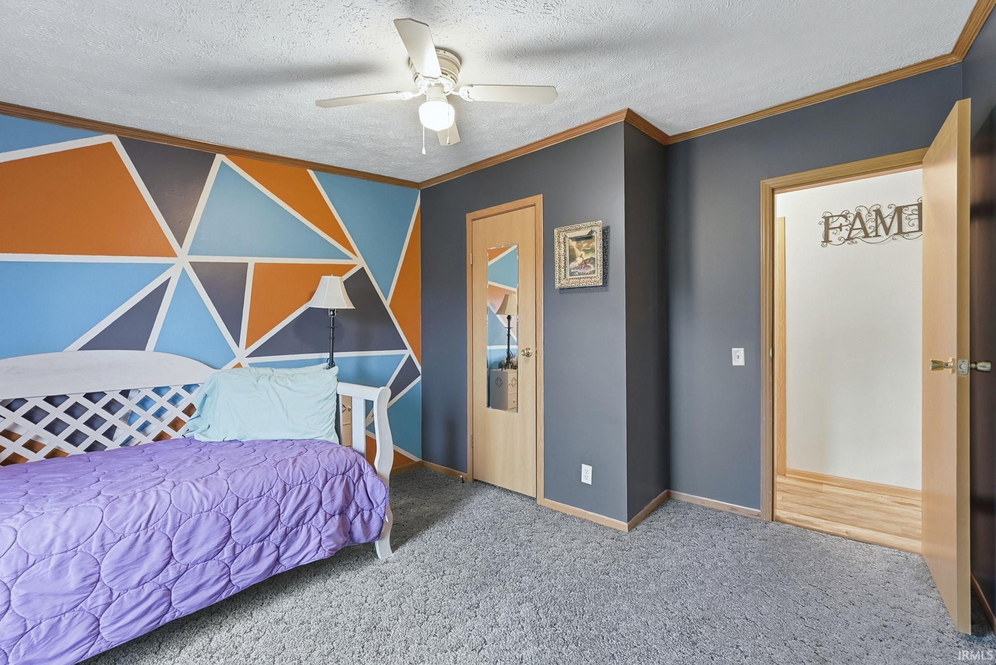 Carpeted bedroom with ornamental molding, a textured ceiling, a ceiling fan, and an accent wall