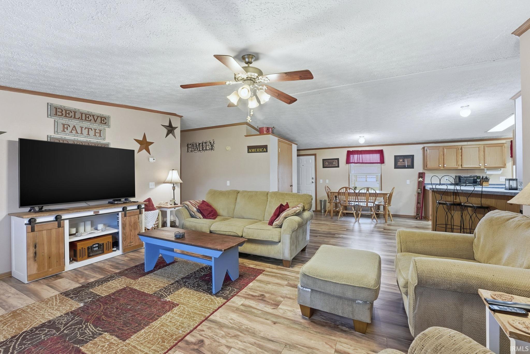 Living area featuring ornamental molding, a ceiling fan, light wood-style flooring, and a textured ceiling