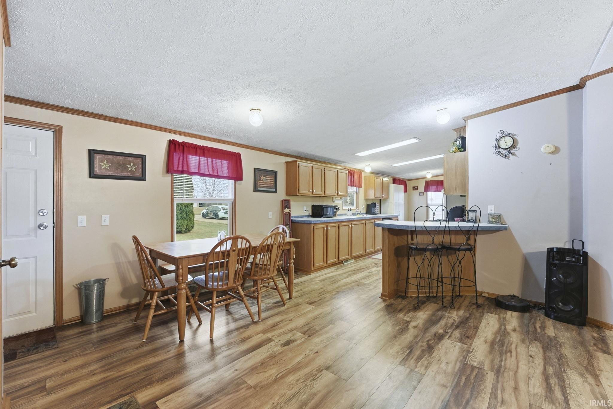 Kitchen with a peninsula, light wood-style floors, crown molding, a textured ceiling, and a breakfast bar