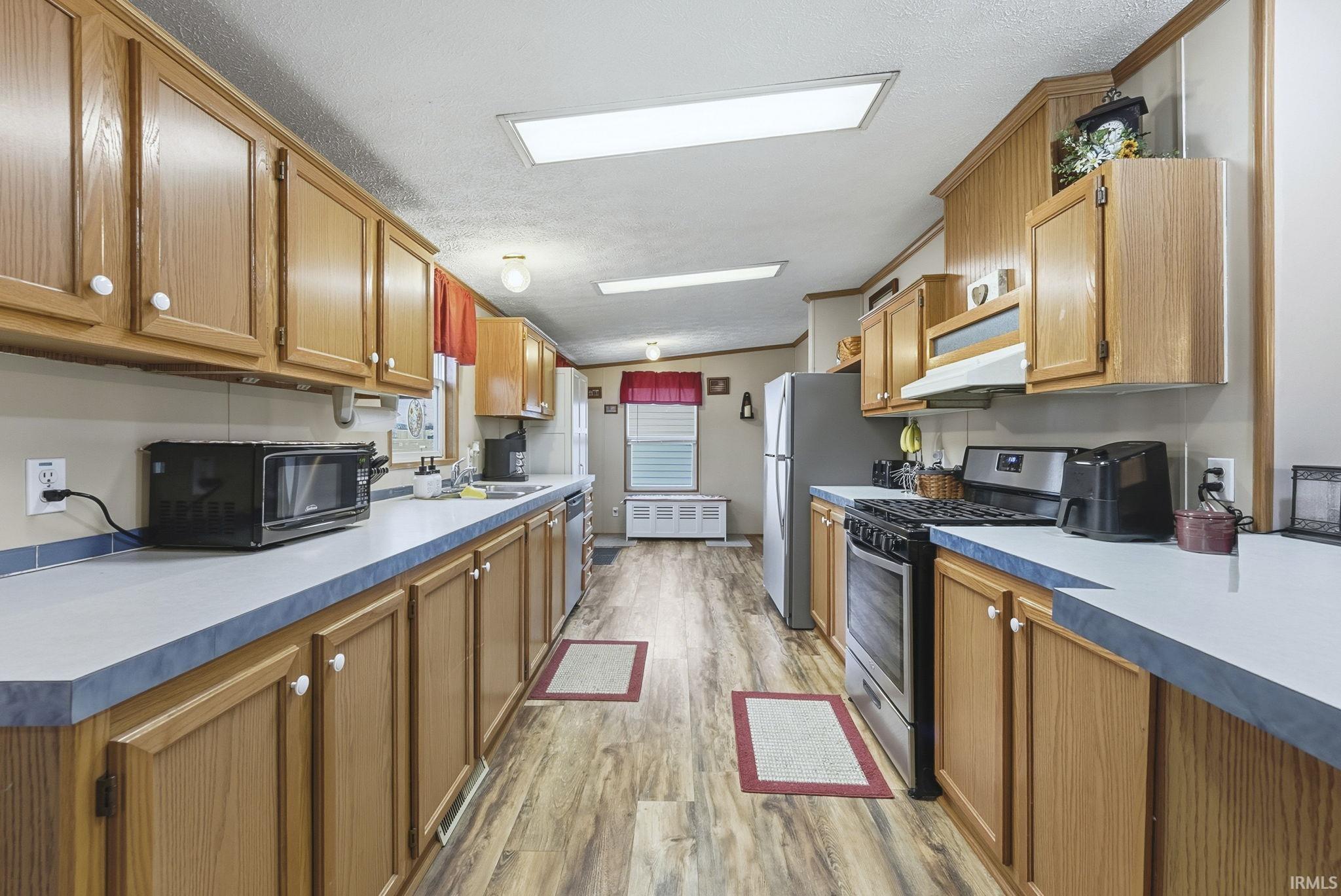 Kitchen with stainless steel appliances, lofted ceiling, brown cabinetry, light wood-type flooring, and light countertops