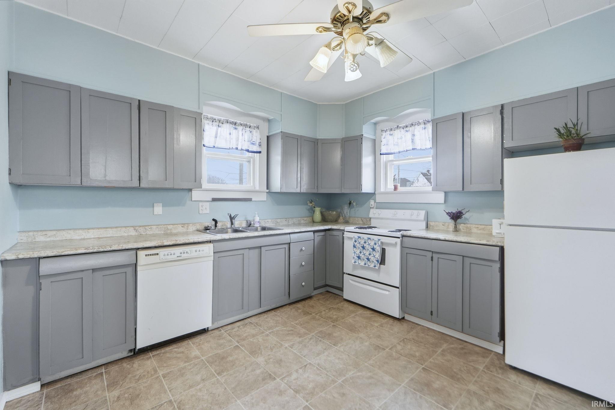 Kitchen with gray cabinetry, white appliances, light countertops, and healthy amount of natural light