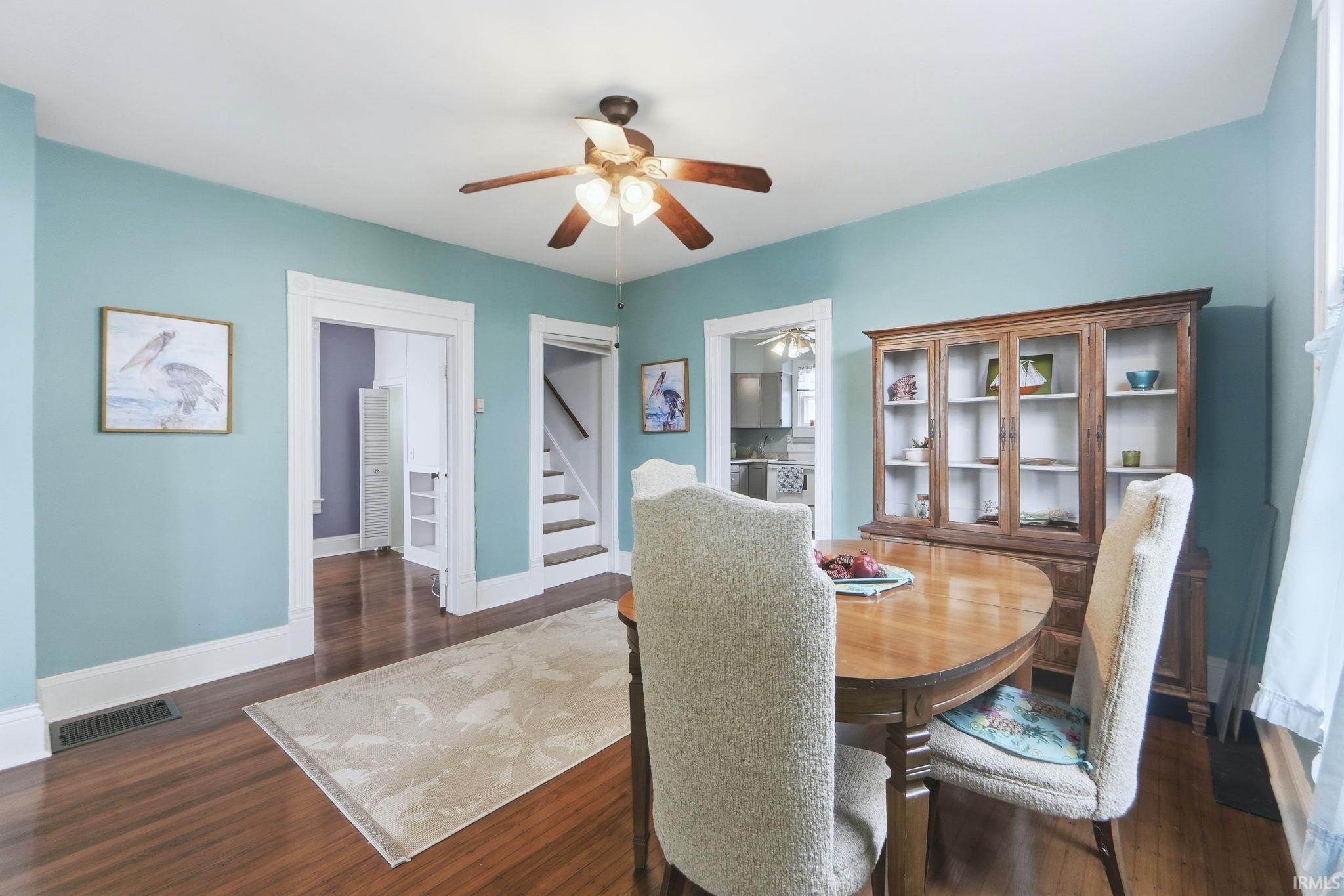 Dining area featuring dark wood finished floors, ceiling fan, and stairs
