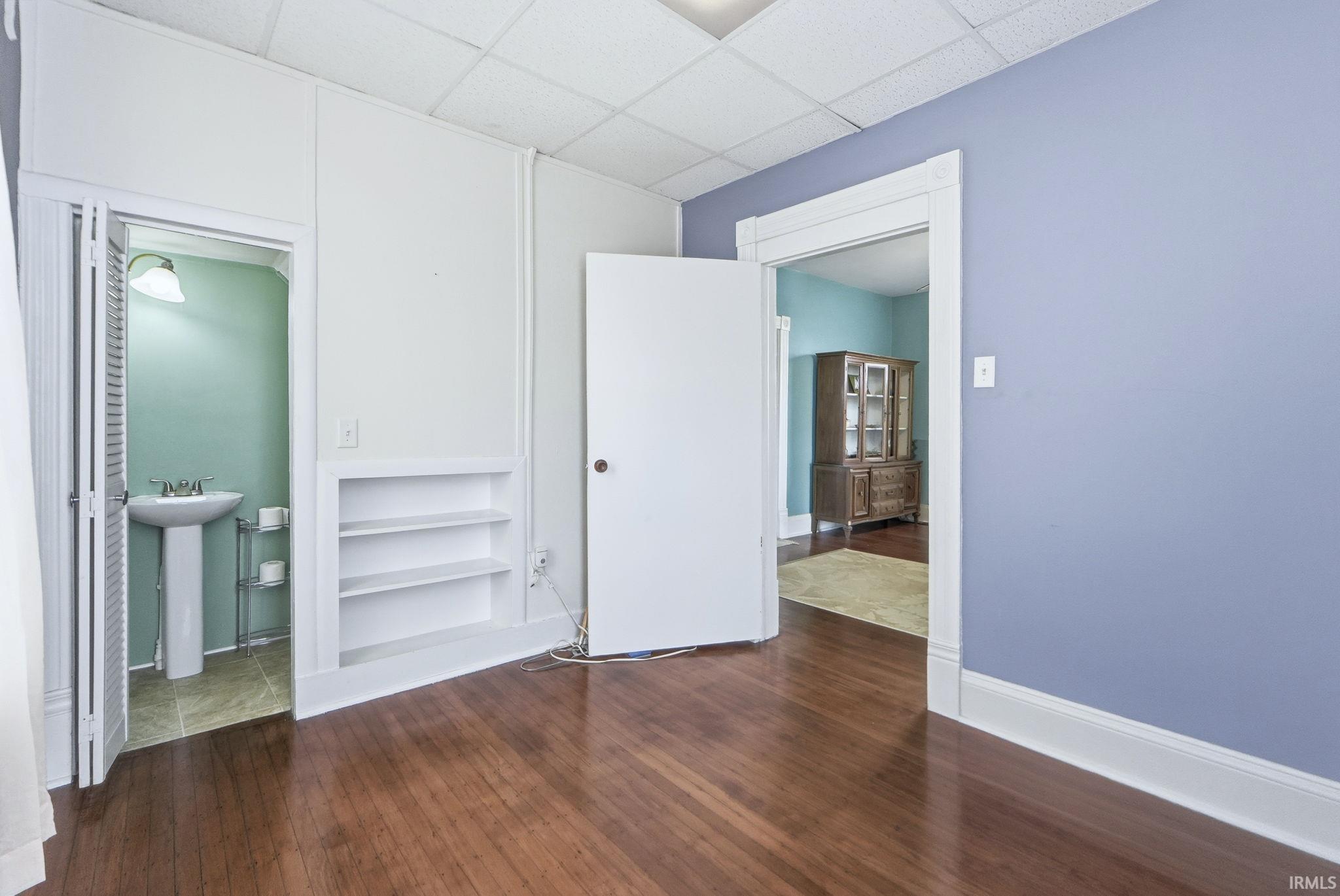 Spare room with dark wood-style floors, built in features, and a drop ceiling