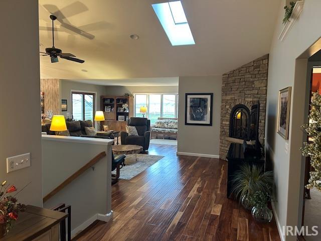 Living area featuring a fireplace, dark wood-style flooring, a skylight, lofted ceiling, and ceiling fan