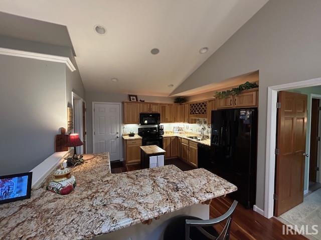 Kitchen with black appliances, a peninsula, a breakfast bar area, light stone countertops, and brown cabinets
